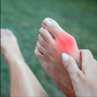 Person holding a foot with a red dot indicating pain on a grassy background